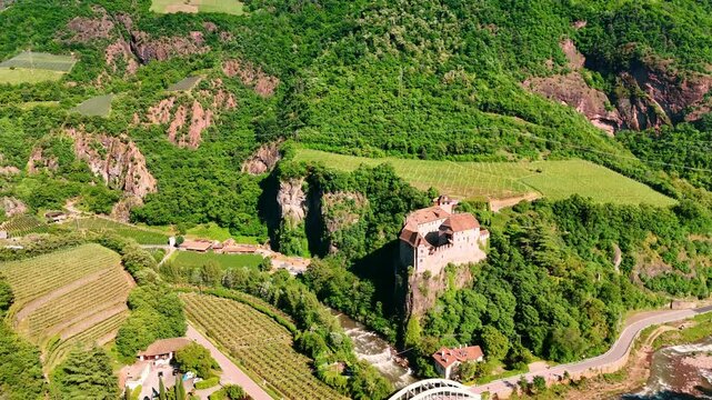 Bright sun illuminates Runkelstein Castle on the unapproachable rock. Green scenery of vineyards in Bolzano, South Tyrol, Italy. Aerial view.