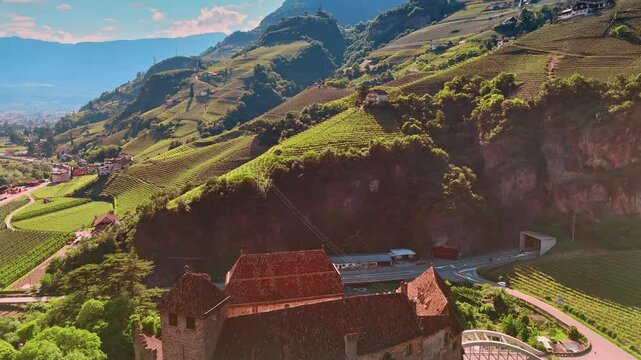 Flying over the Runkelstein Castle and river flower at its foot. Breath-taking scenery of the vineyards covering the slopes of picturesque mountains. Bolzano, South Tyrol, Italy. Aerial view.