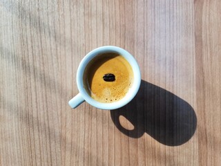 Top view cup of coffee with coffee bean and shadow window light on wooden table.
