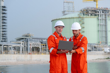 Engineers analyze data on a laptop at a construction site during daytime near industrial facilities