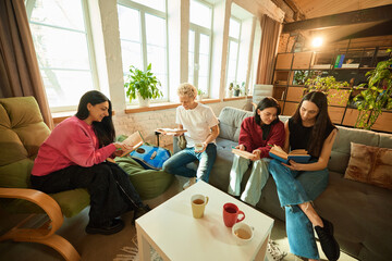 Group of young people sit with books and tea in loft living room enjoying literature and warm atmosphere. Concept of education, leisure, literature, lifestyle, bonding, community, social interaction