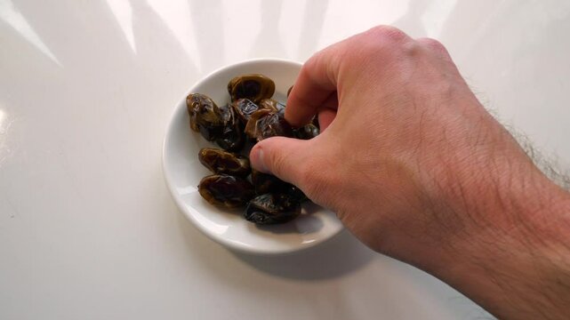 Man eats dried dates, white. Slow motion. Kiwi fruit sliced ​​in a plate.