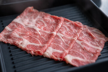 A close-up shot of sliced raw meat, arranged on a plate, ready to be cooked in a hot pot