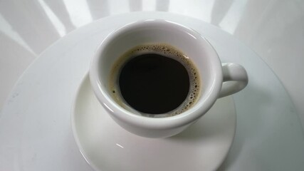 Black instant coffee in a cup on a turntable spins in motion. Top view, slow motion. Coffee drink in a white cup. - Powered by Adobe