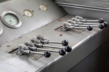 Close-up of a train driver's control panel with multiple levers and analog gauges inside the locomotive cab. The industrial design emphasizes the mechanical and technical aspect of railway transportat