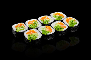 Sushi rolls with salmon, avocado, salad and fish eggs reflecting on black background