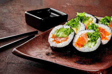 Delicious uramaki sushi rolls with salmon, avocado, and lettuce filling on a brown plate