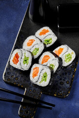 Delicious uramaki sushi rolls with salmon, cucumber, and soy sauce being served on a tray