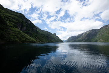 Obraz premium Calm Norwegian fjord under partly cloudy sky and green mountains