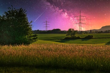 Stunning nightscape with a shooting star and Milky Way over a tranquil field, framed by trees and power lines, capturing the serene beauty of the cosmos