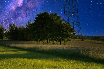 Stunning nightscape with a shooting star and Milky Way over a tranquil field, framed by trees and power lines, capturing the serene beauty of the cosmos