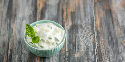 Indian Fresh sauce called Raita with herbs, dahi and sliced cucumber in a bowl on the table.