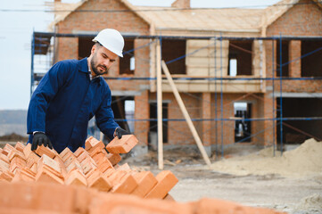 Fototapeta premium Installing brick wall. Construction worker in uniform and safety equipment have job on building