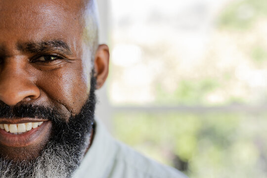 Smiling Senior African American man sitting indoors next to window frame, showing beard, copy space