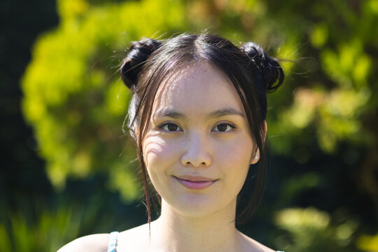 Posing Asian female with two buns gazing at camera in garden, with soft sunlight shadows