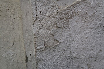 Mur granuleux enduit en blanc avec craquelures et fissures.
