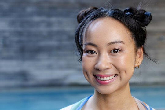 Smiling Asian Chinese woman showing dimples at poolside, with colorful tank top strap, copy space