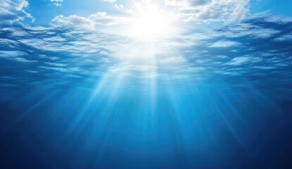 Fototapeta premium Sunlight piercing through deep blue water, reaching into the ocean depths. Clouds appear above