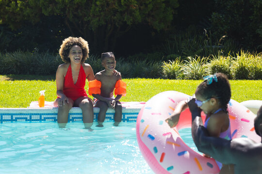 Relaxing African American family sitting poolside in backyard, with pink float and orange arm bands