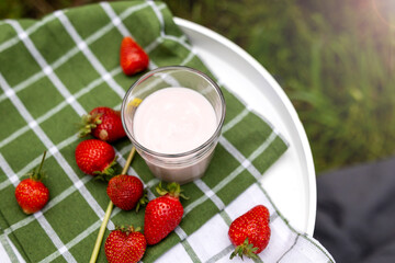 A glass of smooth and creamy strawberry yogurt sitting on a green checkered cloth, representing a...
