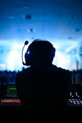Silhouette of a sound technician wearing a headset, working at a control panel during a live event. The background features blue stage lighting, creating a vibrant atmosphere.	