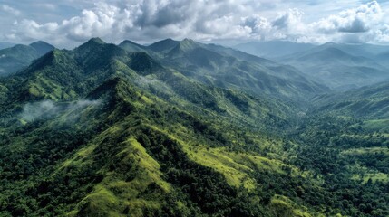 Fototapeta premium Ultra quality image of aerial view of lush green mountain range covered in dense tropical forest with rolling hills and misty valleys under a partly cloudy sky.