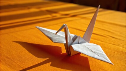 A solitary white origami crane rests on a textured orange surface, casting a shadow that mirrors its graceful form.