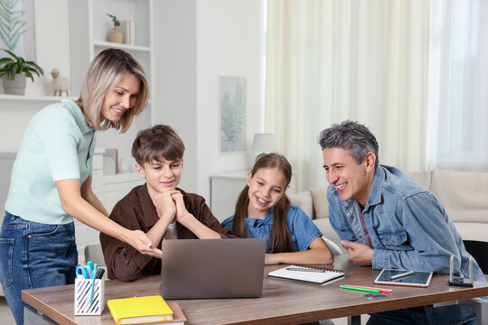 Happy parents and their children doing homework at table indoors