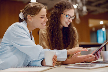 In a cozy coffeeshop setting, two women are collaborating and brainstorming on a project using a...