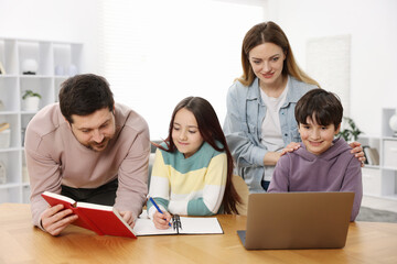 Parents helping their kids with homework at wooden table indoors