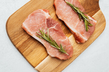 Fresh pork chops with rosemary on a wooden cutting board ready for cooking