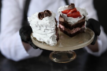 Confectioner with pieces of tasty cake at black marble table in kitchen, closeup