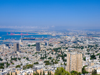 Fototapeta premium A panoramic view of Haifa, Israel, showcasing the city's skyline, modern buildings, green hills, and the bustling port with cargo ships. The vibrant cityscape and coastal views are ideal for travel 