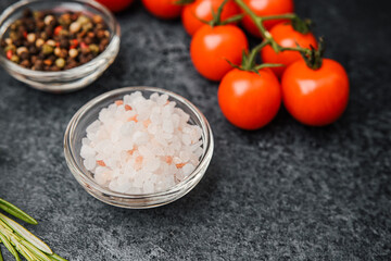 Pink himalayan salt with cherry tomatoes pepper and rosemary on dark background