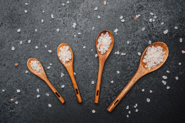 Wooden spoons with coarse pink himalayan salt on black stone surface