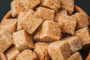 Brown sugar cubes piled in a wooden bowl on a dark surface