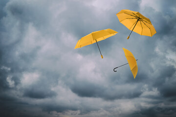 Orange umbrellas flying in cloudy sky. Stormy weather