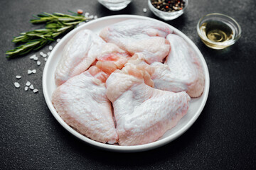 Raw chicken wings with spices herbs and oil on dark stone background