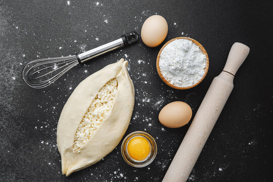 Floured surface with raw khachapuri, eggs and rolling pin for baking