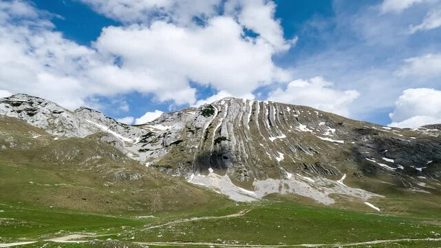 Mountain peaks in Prutas Durmitor Montenegro with snow patches time lapse. Reaching into blue sky and fluffy white clouds, capturing the beauty and tranquility of landscapes outdoors in spring season.