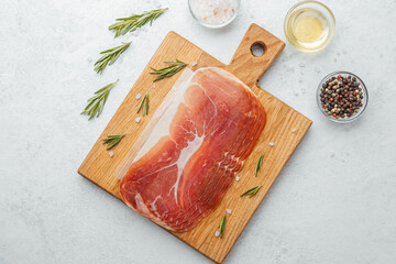 Prosciutto ham slices on cutting board with salt, herbs and spices