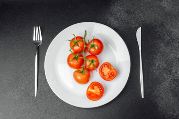 Fresh tomatoes served on a white plate with utensils on a dark surface