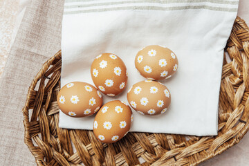 Hand-painted Easter eggs with daisy flowers in a wicker basket. Rustic spring composition for festive celebration.