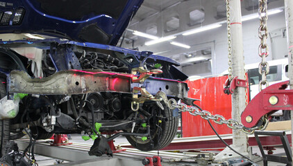 Damaged Car Suspended by Chains on Frame Straightening Rack in Automotive Workshop. Auto Body Frame Machine at Works in Car Service Station