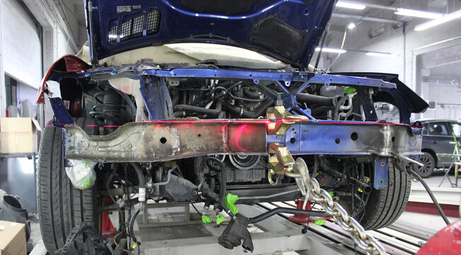 Frame and Parts of Disassembled Front End of Car on Auto Slipway for Chassis Repair. Damaged Car on an Auto Body Tilt Stand Detailed View 