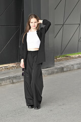 Woman walking in stylish outfit holding sunglasses near modern geometric wall.