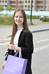 Woman holding a purple shopping bag while standing on a street in a residential area.