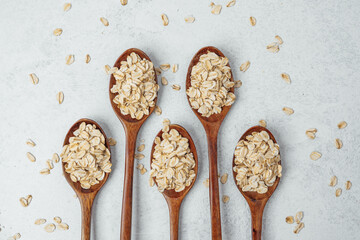 Wooden spoons filled with rolled oats on a light grey background