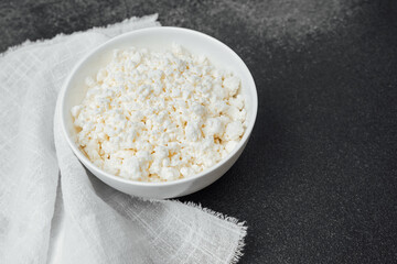 Delicious cottage cheese served in a white bowl on a dark surface