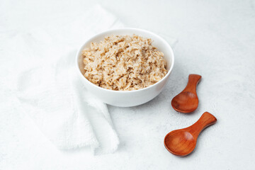Healthy bowl of cooked oatmeal with wooden spoons on white table